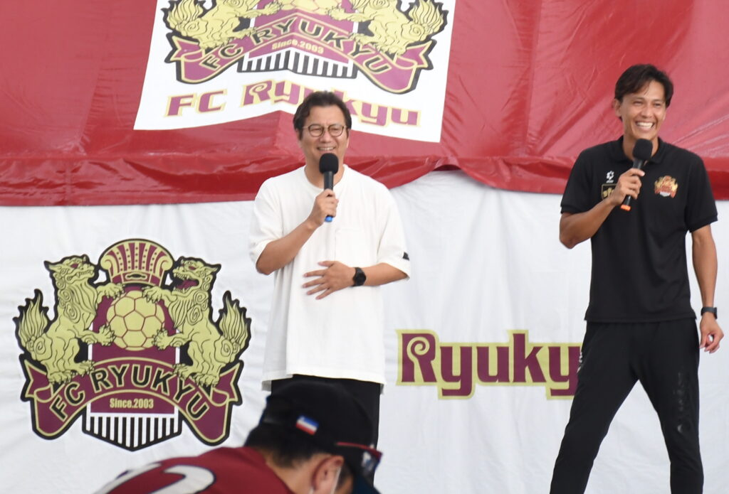 FC琉球の「全島サッカー　一万人祭り」でリフティングイベントに参加する野々村芳和チェアマン（左）と上原慎也クラブコミュニケーター＝8月12日、沖縄市の県総合運動公園